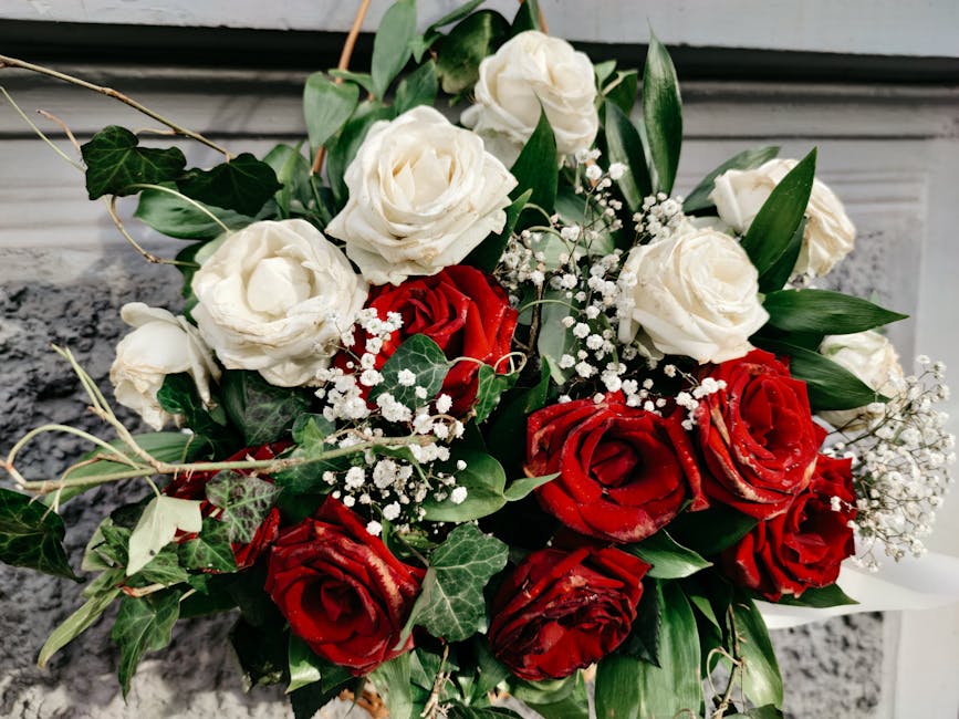 A floral arrangement featuring a bouquet of fresh red and white roses, with the red roses displaying velvety petals and the white roses appearing soft and ruffled. Interspersed among the roses are del