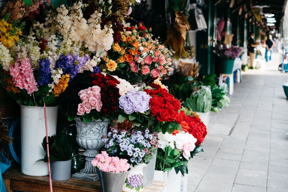 A vibrant outdoor display of freshly arranged flower bouquets at a florist shop on a sidewalk, featuring a variety of colorful blooms including pink, red, purple, yellow, and white roses, lisianthus,