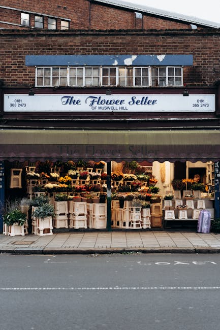 The exterior of The Flower Seller of Muswell Hill, a flower shop on a brick building with a blue sign. The shop’s large display window reveals a vibrant assortment of fresh flower bouquets and flora